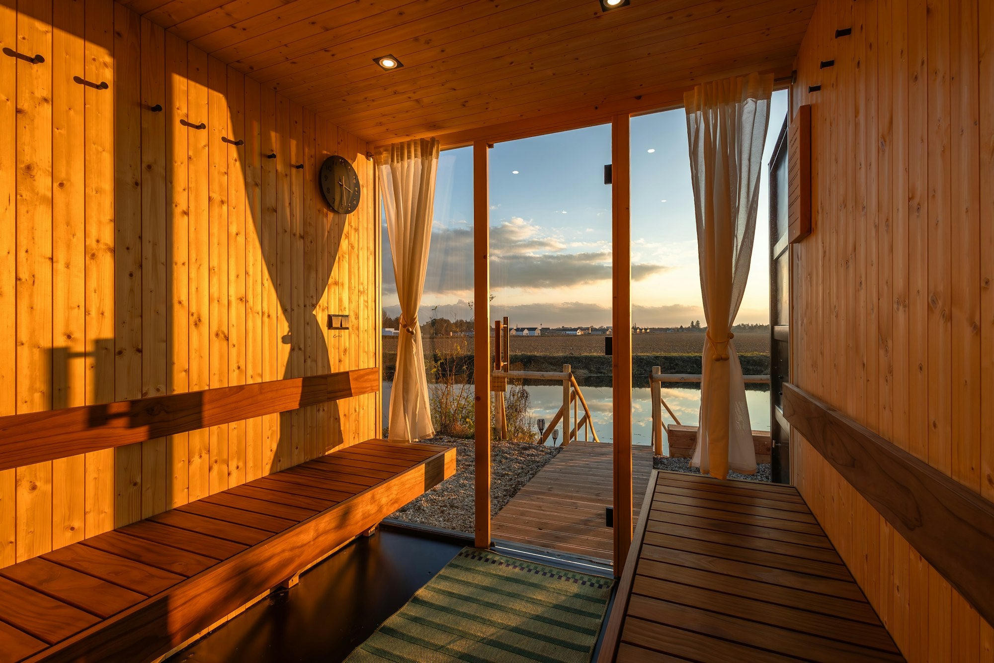 Innenraum einer Holzsauna im Abendlicht mit Blick über einen ruhigen See