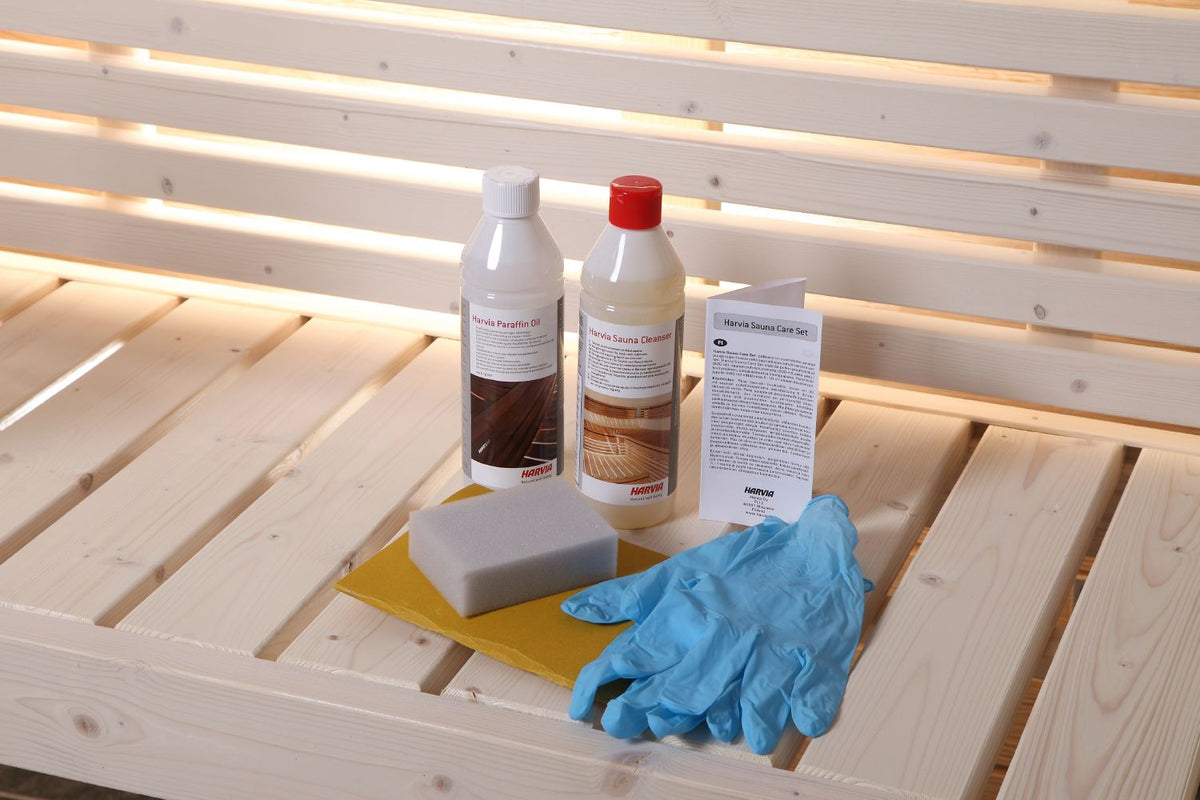 Inhalt des Harvia Sauna Care Set auf einer hellen Saunabank: Paraffinöl, Saunareiniger, Schwamm, Schleifpapier, Handschuhe und Anleitung
