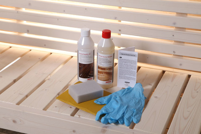 Inhalt des Harvia Sauna Care Set auf einer hellen Saunabank: Paraffinöl, Saunareiniger, Schwamm, Schleifpapier, Handschuhe und Anleitung